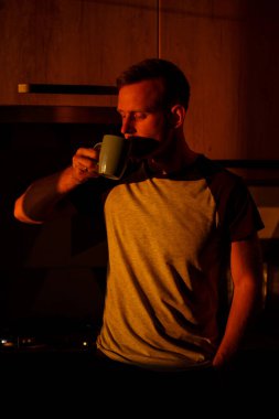 Gün batımında pencerenin önünde duran bir adam mutfakta kahve içiyor.