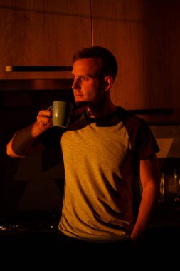 Gün batımında pencerenin önünde duran bir adam mutfakta kahve içiyor.