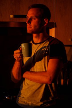 Gün batımında pencerenin önünde duran bir adam mutfakta kahve içiyor.