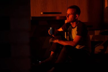 Bir adam gün batımında mutfakta oturur ve kahve içer.