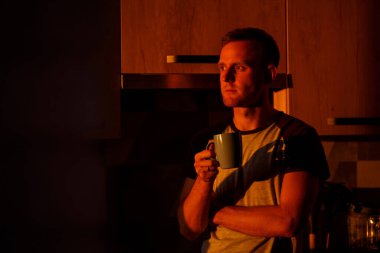 Gün batımında pencerenin önünde duran bir adam mutfakta kahve içiyor.