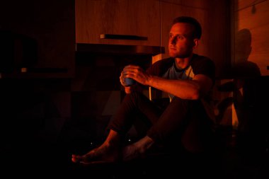 Bir adam gün batımında mutfakta oturur ve kahve içer.