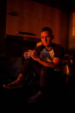 Bir adam gün batımında mutfakta oturur ve kahve içer.