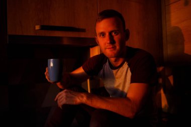 Bir adam gün batımında mutfakta oturur ve kahve içer.