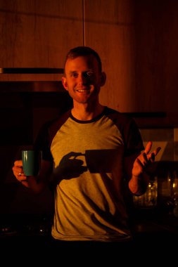 Gün batımında pencerenin önünde duran bir adam mutfakta kahve içiyor.