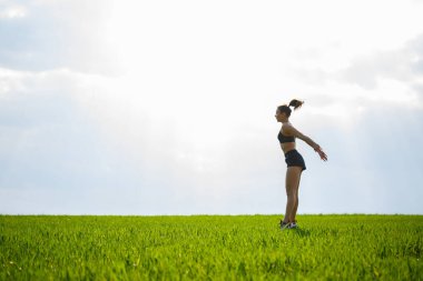 Genç atletik kız gün batımından önce çimlerin üzerinde zıplıyor. Egzersiz, spor, sağlıklı yaşam tarzı.