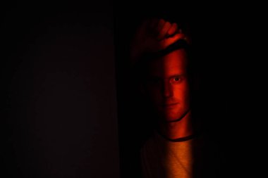 Dramatik, zarif, yüzünde ışık saçan genç bir adam stüdyodaki kameraya bakıyor.