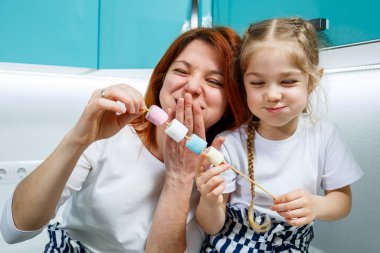 Anne ve kızı turkuaz mutfakta marşmelov yiyor. Hoş aile ilişkileri. Mutlu aile kavramı, mutlu ebeveynler ve çocuklar