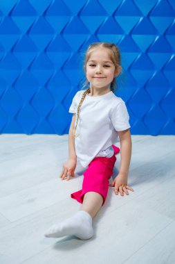 Mavi arka planda beyaz tişörtlü, at kuyruklu küçük bir kız yerde sicim içinde oturuyor ve gülümsüyor. Çocukların duyguları işgal noktası, eğlence.