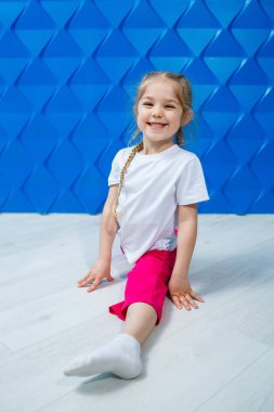 Mavi arka planda beyaz tişörtlü, at kuyruklu küçük bir kız yerde sicim içinde oturuyor ve gülümsüyor. Çocukların duyguları işgal noktası, eğlence.