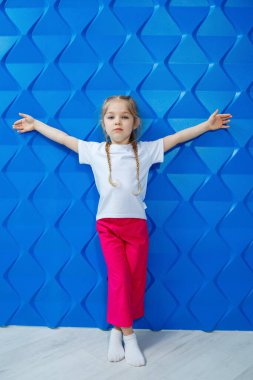 Mavi arka planda beyaz tişörtlü sarı saçlı bir kız. Gülümser ve ellerini sallar.