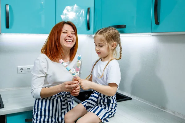 Mom and daughter in the turquoise kitchen are playing with marshmallows. Lovely family relationships. Happy family concept