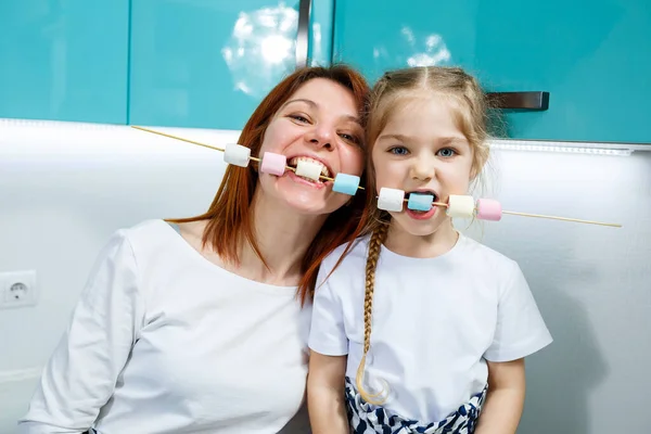 Mom with daughter in the turquoise kitchen eat marshmallows. Lovely family relationships. Happy family concept, happy parents and children