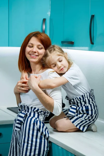 Mom and daughter in the kitchen cook, eat, hug. The concept of a happy family. Relations between parents and children, jolly childhood