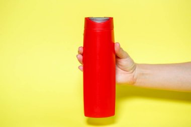 Elinde jöle şampuanıyla kırmızı şişe ya da sarı arka planda sıvı sabun.