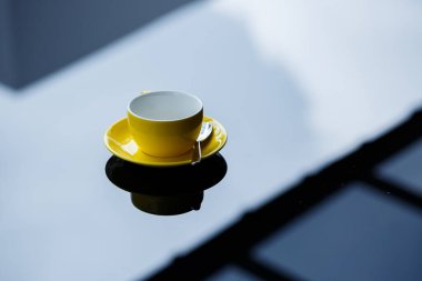 Kahve ya da çay için sarı kupa, cam masanın üstünde çay tabağı..