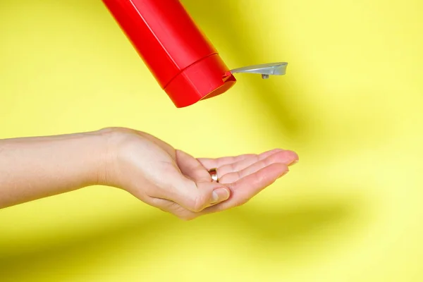Red bottle in hands with gel shampoo or liquid soap on a yellow background