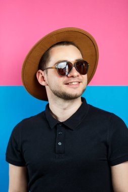 Siyah polo giyen, güneş gözlüklü ve kahverengi şapkalı zarif bir adamın stüdyo portresi. Şık bir adam. Yüzünde bir gülümseme. Bir erkek fotoğrafı için görüntü