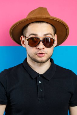 Siyah polo giyen, güneş gözlüklü ve kahverengi şapkalı zarif bir adamın stüdyo portresi. Şık bir adam. Yüzünde bir gülümseme. Bir erkek fotoğrafı için görüntü