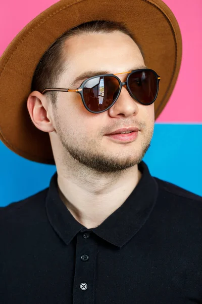 Siyah polo giyen, güneş gözlüklü ve kahverengi şapkalı zarif bir adamın stüdyo portresi. Şık bir adam. Yüzünde bir gülümseme. Bir erkek fotoğrafı için görüntü