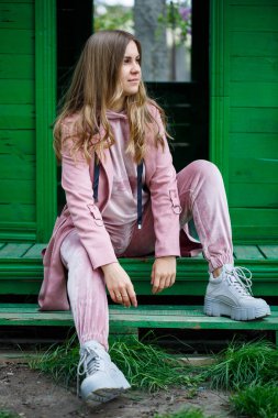 Avrupa görünümlü sarı saçlı şık genç kız merdivenlerde oturuyor, pembe bir takım elbise giyiyor, modern kadın modası, gündelik kıyafetler.