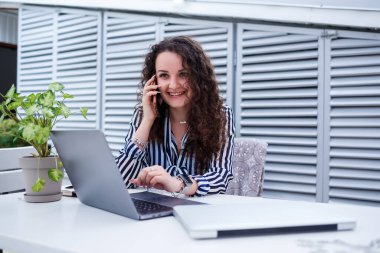 Gülümseyen başarılı genç bir kadın telefonda konuşuyor, terasta dizüstü bilgisayarla çalışıyor, iş toplantısındaki bir kız. İş konsepti