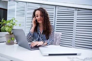 Gülümseyen başarılı genç bir kadın telefonda konuşuyor, terasta dizüstü bilgisayarla çalışıyor, iş toplantısındaki bir kız. İş konsepti