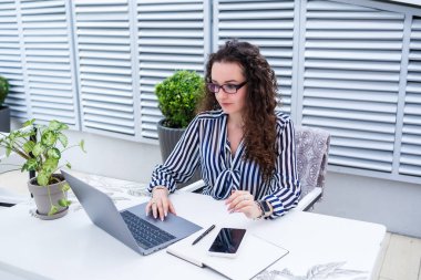 Başarılı genç bayan girişimci gülümseyerek bir bilgisayar ekranına bakıyor, açık kafe terasında dizüstü bilgisayar kullanarak çalışıyor.