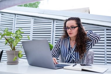 Başarılı genç bayan girişimci gülümseyerek bir bilgisayar ekranına bakıyor, açık kafe terasında dizüstü bilgisayar kullanarak çalışıyor.