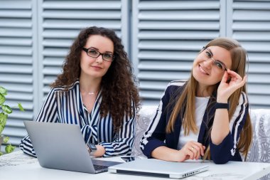 İki iş kadını parlak bir kafede dizüstü bilgisayarları ve iş belgeleriyle oturup ciddi insanlarla konuşuyorlar. Ofis çalışanları kahve molalarında oturuyorlar ve çalışıyorlar. Bir kafede iş görüşmesi.