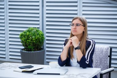 Laptopla çalışan uzun saçlı genç bir kadın bir kafedeki terasta oturuyor. İş geliştirme konsepti, öğle yemeği molasında bir fincan kahve üzerinde çalışan kız.