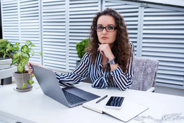 Dizüstü bilgisayarda çalışan güzel genç bir kadın ve dışarıda bir kafede otururken gülümsüyor. Genç bir kadın iş için laptop kullanıyor. Açık bir kafede dizüstü bilgisayarda çalışan serbest çalışan bir kadın..