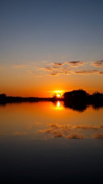 Gölde gün batımı, ağaçların arkasında güneş batışı ve suda güzel yansımalar.