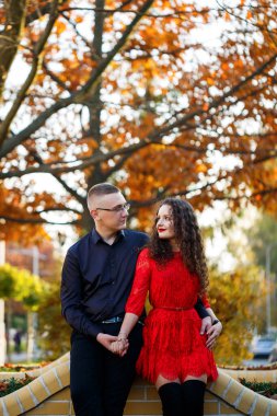 Siyah tişörtlü bir adam ve sonbahar caddesinde kırmızı elbiseli bir kız.