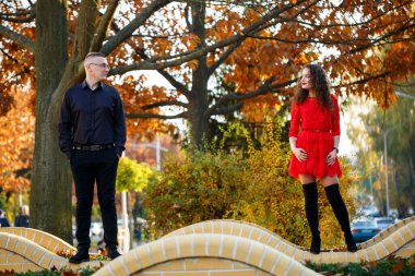 Siyah tişörtlü bir adam ve sonbahar caddesinde kırmızı elbiseli bir kız.