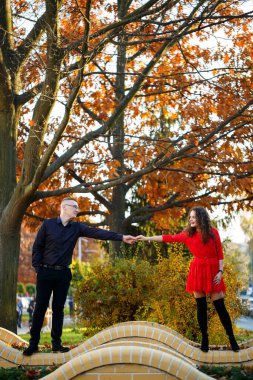 Siyah tişörtlü bir adam ve sonbahar caddesinde kırmızı elbiseli bir kız.