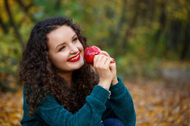 Sonbahar ormanında elinde elma, yeşil kazaklı bir kız.