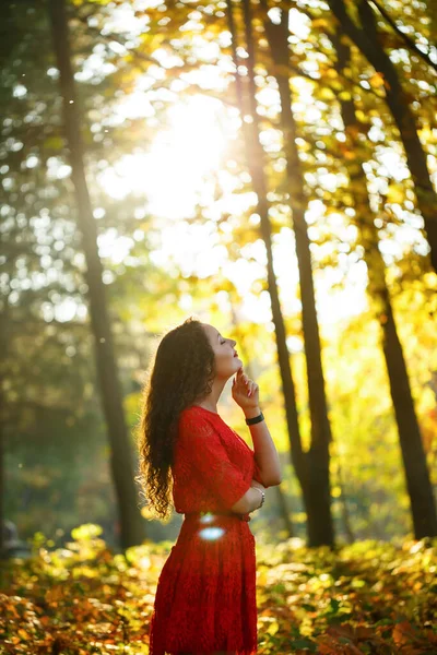 Kıvırcık saçlı kız sonbahar ormanında kırmızı elbiseli.