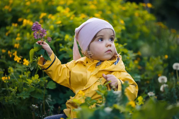 写真は幸せな子供の女の子が黄色のジャケットと白い帽子の牧草地で遊んで着て 花は子供と草に囲まれ 日没の間にフィールドで遊んでいます 幼少期の概念 — ストック写真