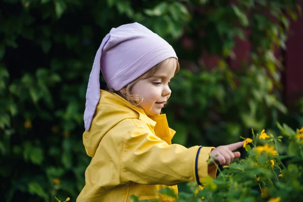 穿着黄色夹克的漂亮姑娘在草地上采花 一个孩子站在春花丛中鲜绿的草地上 一个小孩用第一束黄色野花做一束花 — 图库照片