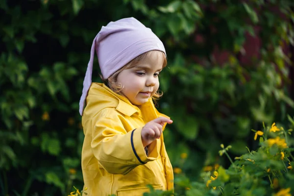 一个穿着黄色夹克的小女孩站在黄花旁 — 图库照片