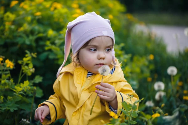 写真は幸せな子供の女の子が黄色のジャケットと白い帽子の牧草地で遊んで着て 花は子供と草に囲まれ 日没の間にフィールドで遊んでいます 幼少期の概念 — ストック写真