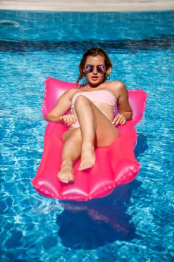 Seksi kadın model dinleniyor ve havuzda şiltede güneşleniyor. Pembe bikinili bir kadın şişme pembe bir yatakta yüzüyor. spf ve güneş kremi