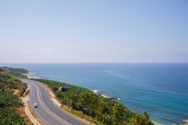Boş bir asfalt yol güneşli bir yaz gününde nefes kesici kıyı şeridi boyunca esiyor. Berrak mavi gökyüzüne ve sakin Akdeniz 'e bakan kıyı yolunun muhteşem bir görüntüsü..