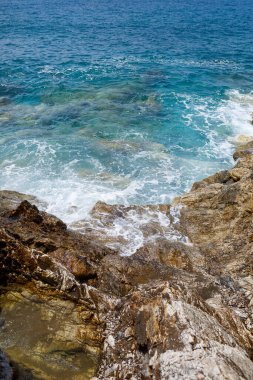 Mavi Akdeniz 'in harika manzarası. Güneşli kayalar, köpüklü dalgalar ve su sıçraması. Dalga kıyıdaki kayalara çarpar.