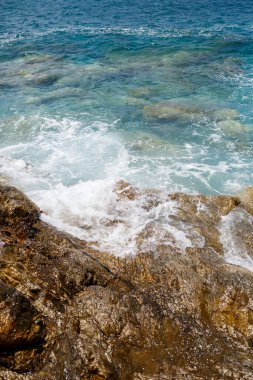 Mavi Akdeniz 'in harika manzarası. Güneşli kayalar, köpüklü dalgalar ve su sıçraması. Dalga kıyıdaki kayalara çarpar.