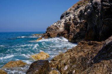 Mavi Akdeniz 'in harika manzarası. Güneşli kayalar, köpüklü dalgalar ve su sıçraması. Dalga kıyıdaki kayalara çarpar.