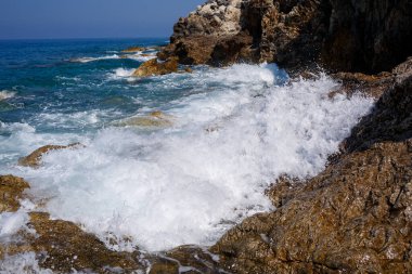 Mavi Akdeniz 'in harika manzarası. Güneşli kayalar, köpüklü dalgalar ve su sıçraması. Dalga kıyıdaki kayalara çarpar.