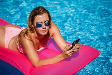 Mayolu seksi bir kadın havuzda pembe şişme bir şiltenin üzerinde yatıyor. Sıcak ve güneşli bir yaz gününde havuz kenarında rahatla. Tatil kavramı