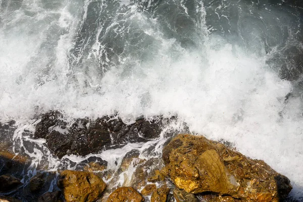 Mavi Akdeniz 'in harika manzarası. Güneşli kayalar, köpüklü dalgalar ve su sıçraması. Dalga kıyıdaki kayalara çarpar.